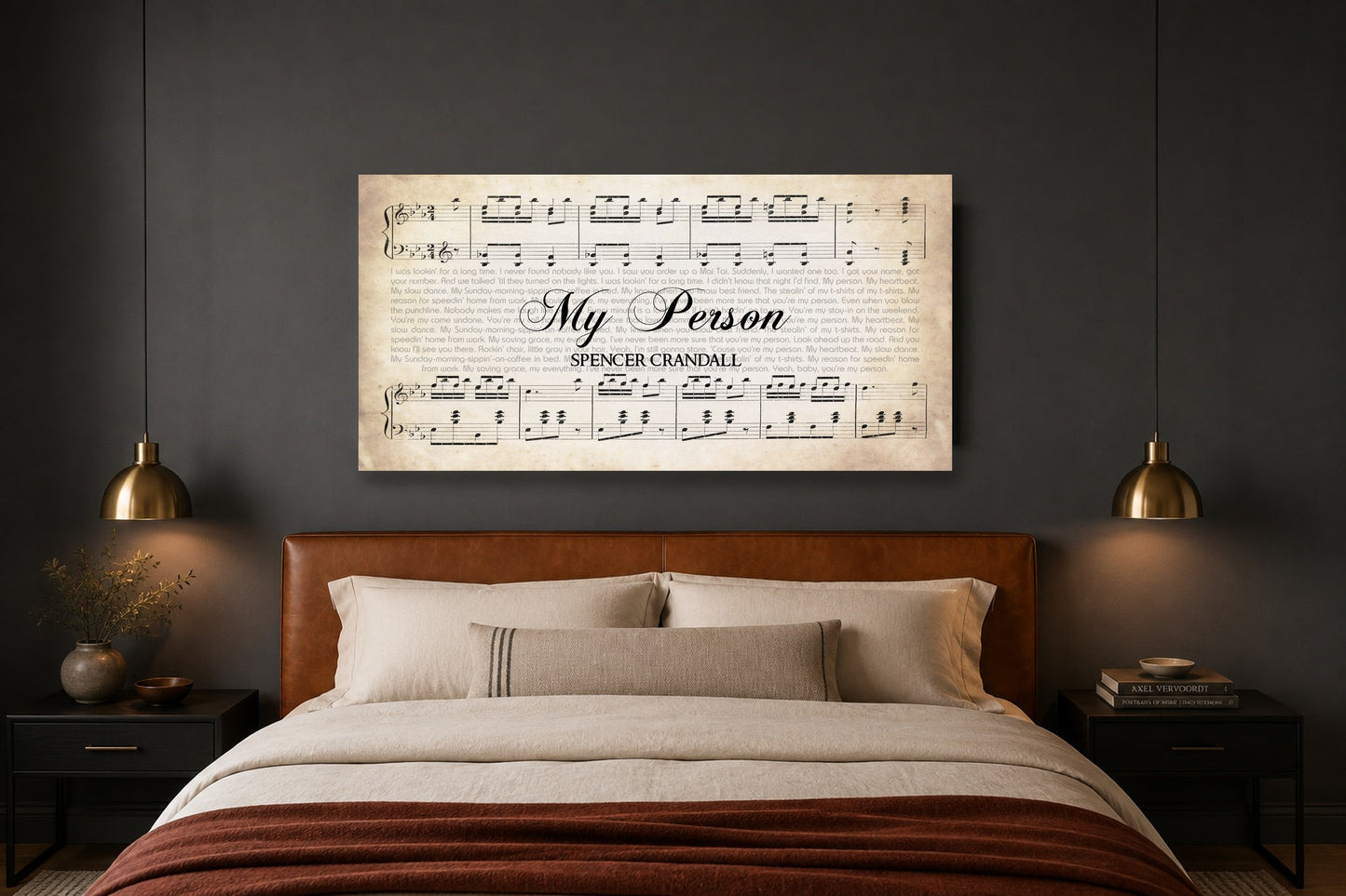Anniversary song lyrics canvas above a caramel leather headboard in a charcoal bedroom with brass pendant lights