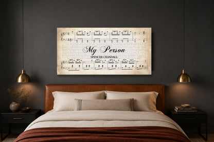 Anniversary song lyrics canvas above a caramel leather headboard in a charcoal bedroom with brass pendant lights