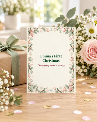 Funny Baby's First Christmas card styled with a gift and flowers