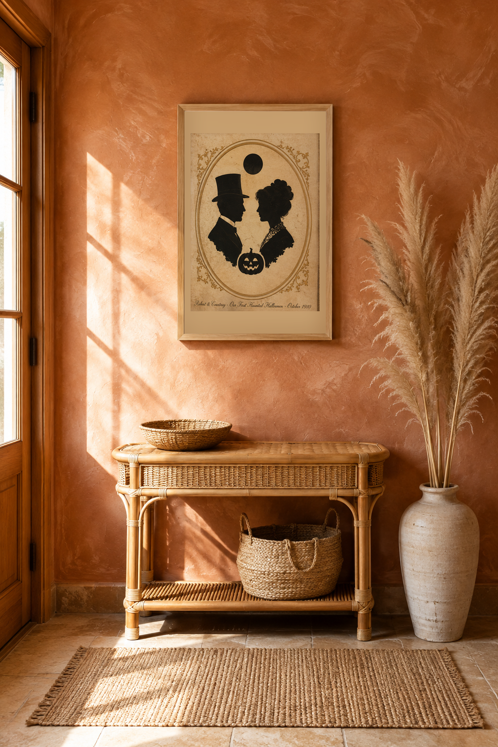 Vintage 1910 couple silhouette Halloween wall art in an oak frame on a terracotta clay plaster entryway wall above a rattan console with pampas grass and a jute basket