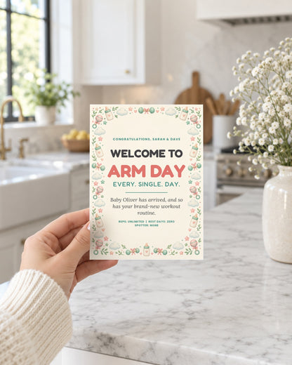 Hand holding the Arm Day new baby card in a bright kitchen