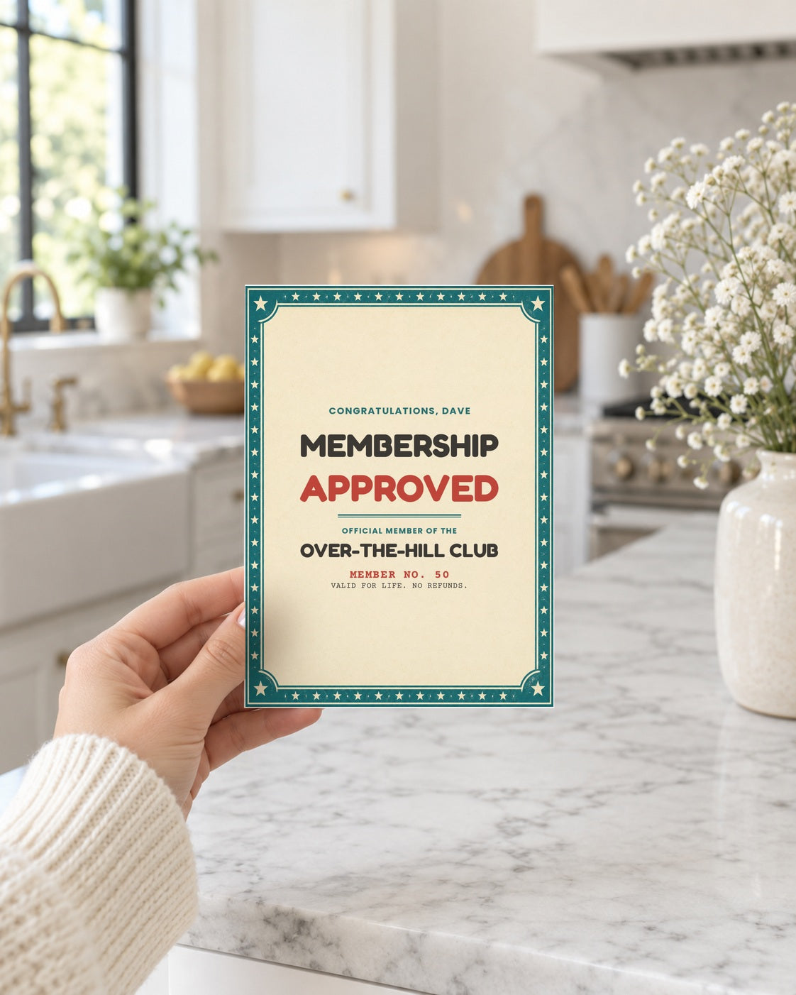 Hand holding the membership approved birthday card in a bright kitchen