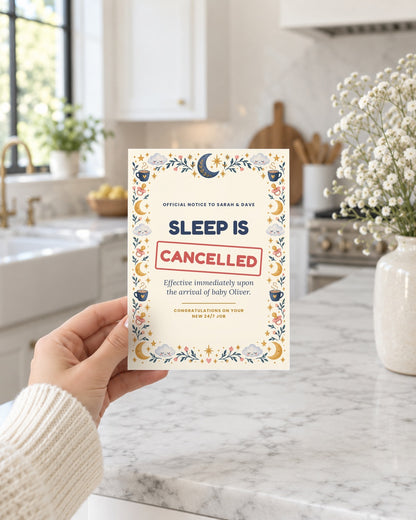 Hand holding the Sleep Is Cancelled new baby card in a kitchen