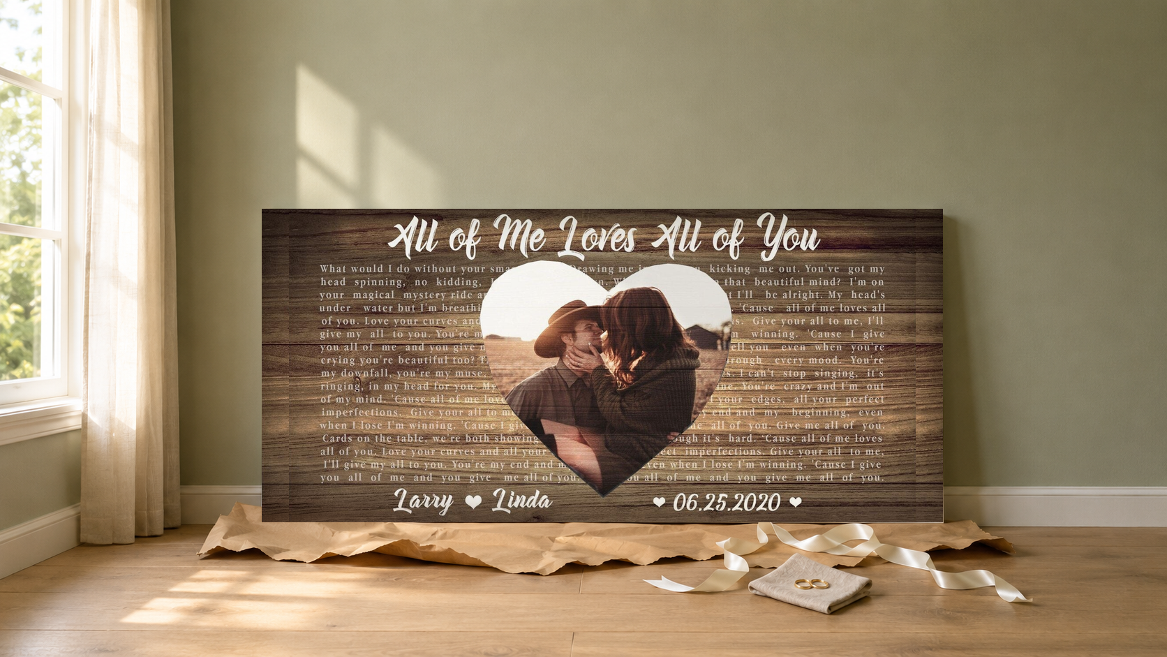 First anniversary song lyric canvas gift unwrapped on an oak floor with kraft paper, satin ribbon and wedding rings