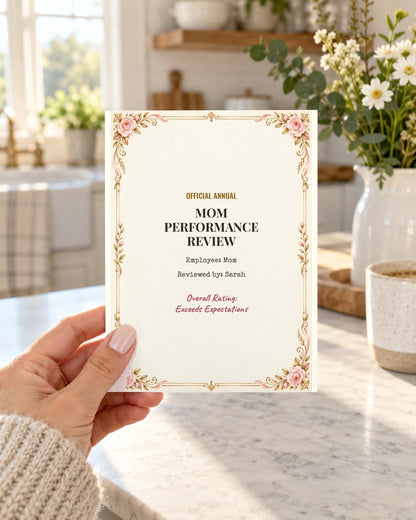Hand holding the Mom Performance Review card in a sunny kitchen
