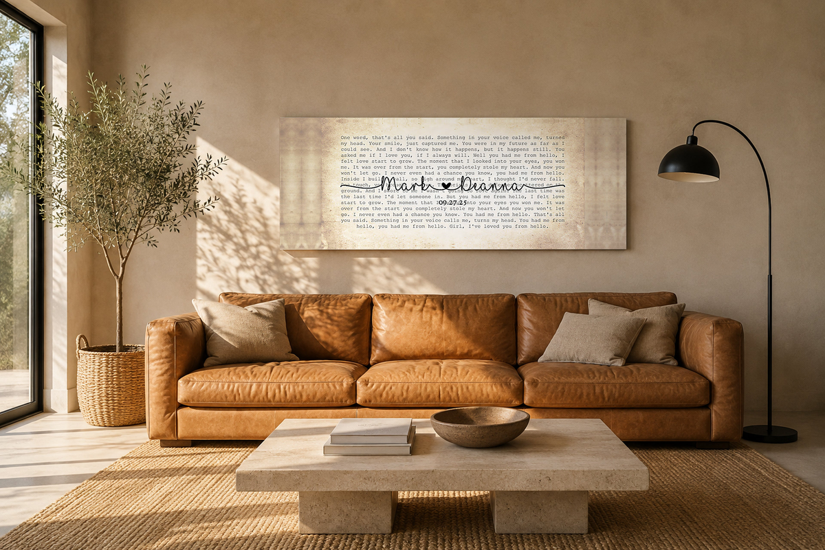 Personalized first dance song lyric canvas hung above a camel leather sofa in a warm sunlit living room with an olive tree and jute rug