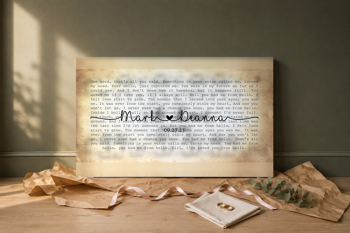 Custom wedding song lyric canvas unwrapped as a gift on a pale oak floor with kraft paper, blush ribbon, gold wedding bands and eucalyptus