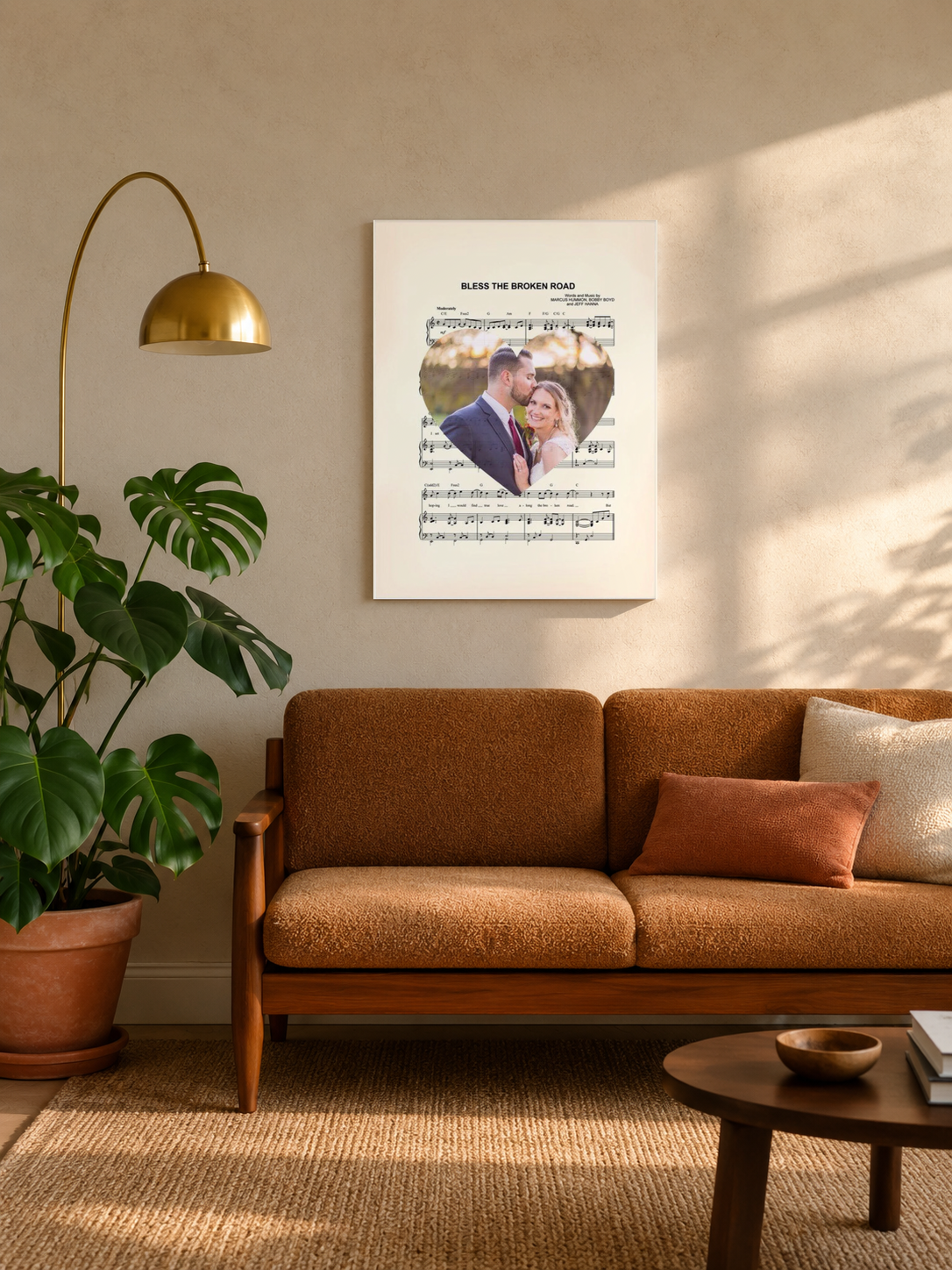Custom song lyrics sheet music print with wedding photo heart, hung in a cozy mid-century living room above a caramel sofa with a brass floor lamp and monstera