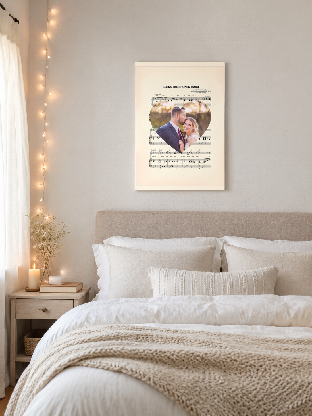 Personalized song lyrics photo print hanging above a linen bed in a serene neutral master bedroom with string lights and a lit candle