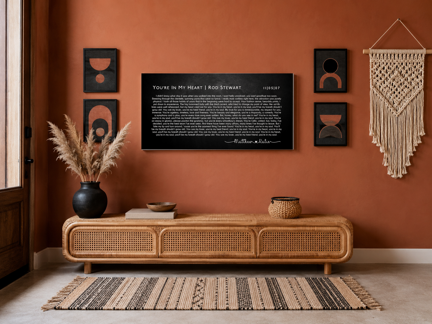 Wide song lyric wall art on a terracotta boho gallery wall above a rattan console with pampas grass