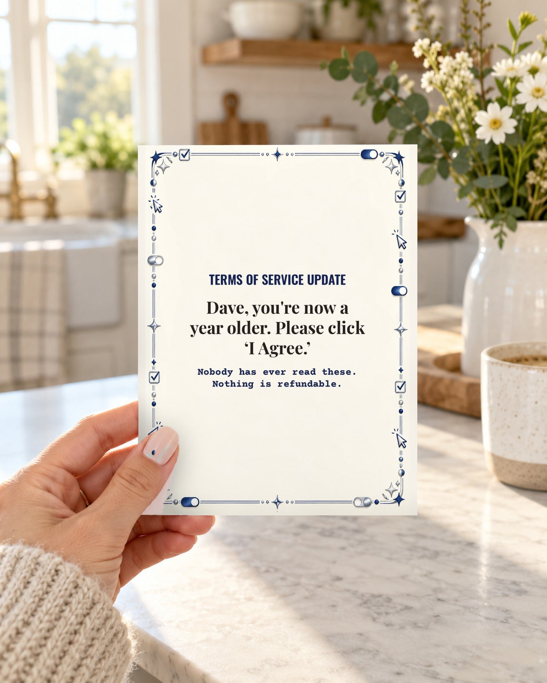 Hand holding the funny Terms of Service Update birthday card for husband in a bright kitchen