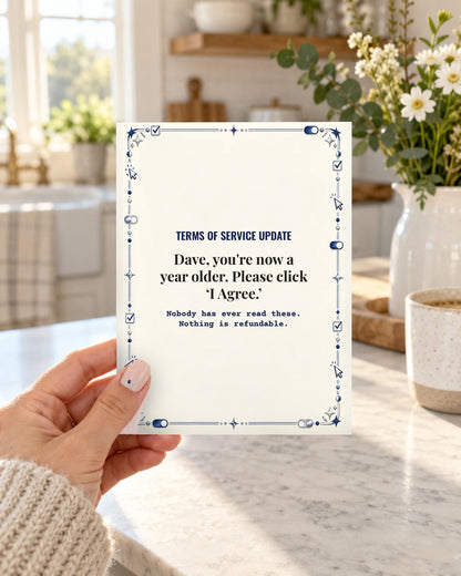Hand holding the funny Terms of Service Update birthday card for husband in a bright kitchen